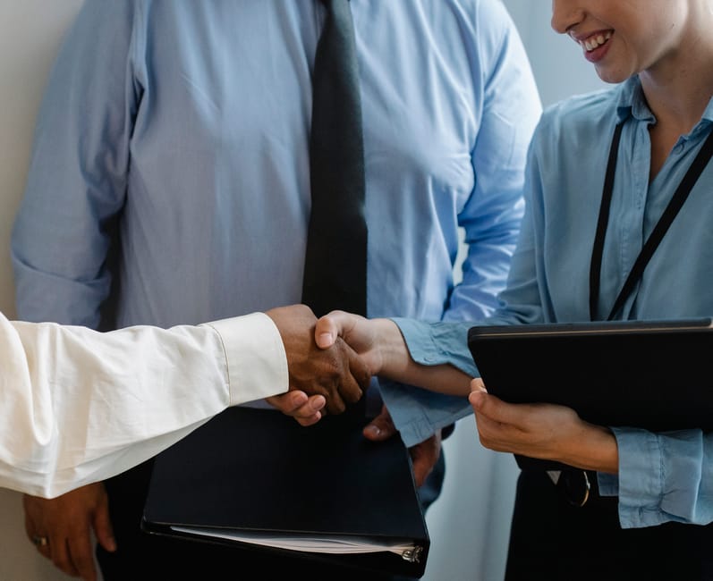 Crop unrecognizable diverse partners in formal clothes with documents shaking hands during business meeting in office
